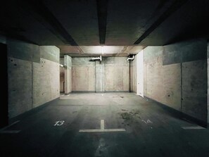 A dimly lit parking garage with concrete walls and a concrete floor marked with parking spaces. - 1BR La Florida - Free Parking, Pool & Metro (La Florida)