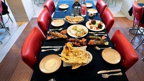 Une table à manger dressée avec différents plats, des chaises à revêtement rouge et une nappe bleue.