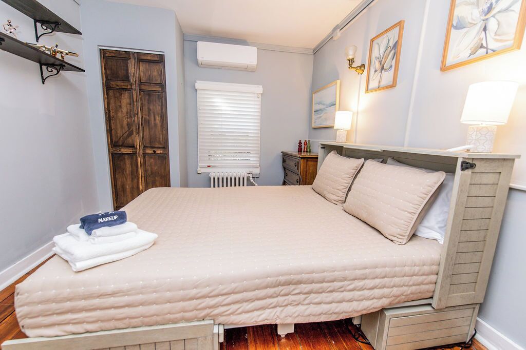 Una cama bien hecha con cubrecama acolchada, una mesita de noche con lámpara y un aire acondicionado de pared.