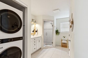 Un baño moderno con lavadora integrada, mampara de vidrio y una pequeña planta en un estante.