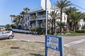 Un edificio frente a la playa con balcones, palmeras y un letrero que indica acceso a la playa.