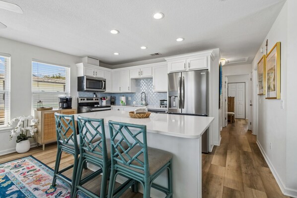 A modern kitchen with white cabinetry, stainless steel appliances, and a central island with bar stools. - Updated 3-bedroom, 2 bath coastal cottage across from the beach UNIT A (Fernandina Beach)