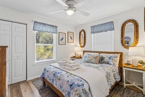 A bedroom with a bed, bedside tables, a ceiling fan, and a large mirror. - Updated 3-bedroom, 2 bath coastal cottage across from the beach UNIT A (Fernandina Beach)
