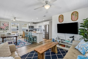 A modern kitchen with white cabinets, stainless steel appliances, and a large flat-screen TV mounted on the wall. - Updated 3-bedroom, 2 bath coastal cottage across from the beach UNIT A (Fernandina Beach)