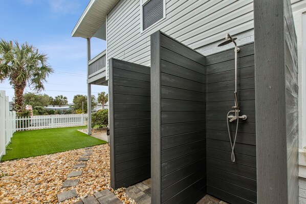 A modern outdoor shower area with a metal hose and a white fence in the background. - Updated 3-bedroom, 2 bath coastal cottage across from the beach UNIT A (Fernandina Beach)