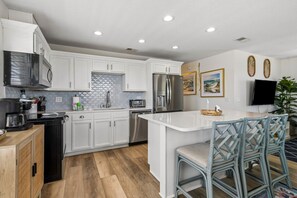 A modern kitchen with white cabinetry, stainless steel appliances, and a central island with bar stools. - Updated 3-bedroom, 2 bath coastal cottage across from the beach UNIT A (Fernandina Beach)