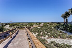 A wooden boardwalk leading to the beach with a clear view of the ocean and palm trees. - Updated 3-bedroom, 2 bath coastal cottage across from the beach UNIT A (Fernandina Beach)