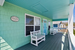 A porch with two white benches, a blue door, and a sign welcoming visitors to the property. - Updated 3-bedroom, 2 bath coastal cottage across from the beach UNIT A (Fernandina Beach)