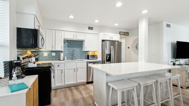 A modern kitchen with white cabinets, stainless steel appliances, and a central island with bar stools. - Updated 3-bedroom, 2 bath coastal cottage across from the beach UNIT B (Fernandina Beach)