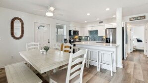 A modern kitchen with white cabinetry, a central island, and a dining area with a white table and chairs. - Updated 3-bedroom, 2 bath coastal cottage across from the beach UNIT B (Fernandina Beach)