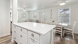 A modern kitchen with white cabinetry, a central island, and a dining area with white chairs. - Updated 3-bedroom, 2 bath coastal cottage across from the beach UNIT B (Fernandina Beach)