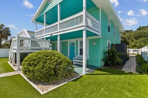 A two-story house with a green exterior, a front porch, and a small front yard with a bush.