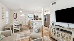 A modern living room with a flat-screen TV, a dining area with white furniture, and a kitchen with stainless steel appliances. - Updated 3-bedroom, 2 bath coastal cottage across from the beach UNIT B (Fernandina Beach)