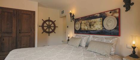 A bedroom with a large bed, a wooden wardrobe, a ship's wheel, a world map painting, and wall-mounted lamps.