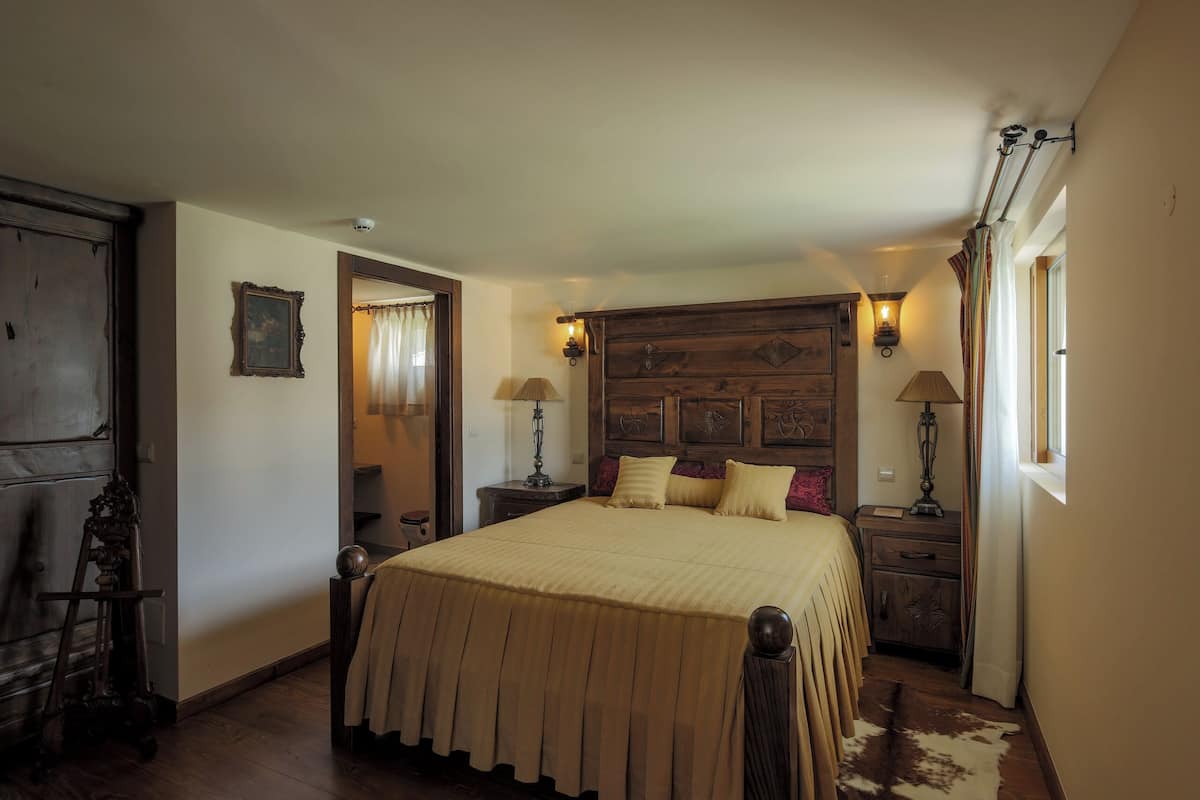 Une chambre à coucher avec un grand lit, une tête de lit en bois, deux tables de chevet avec des lampes, un miroir et une porte.