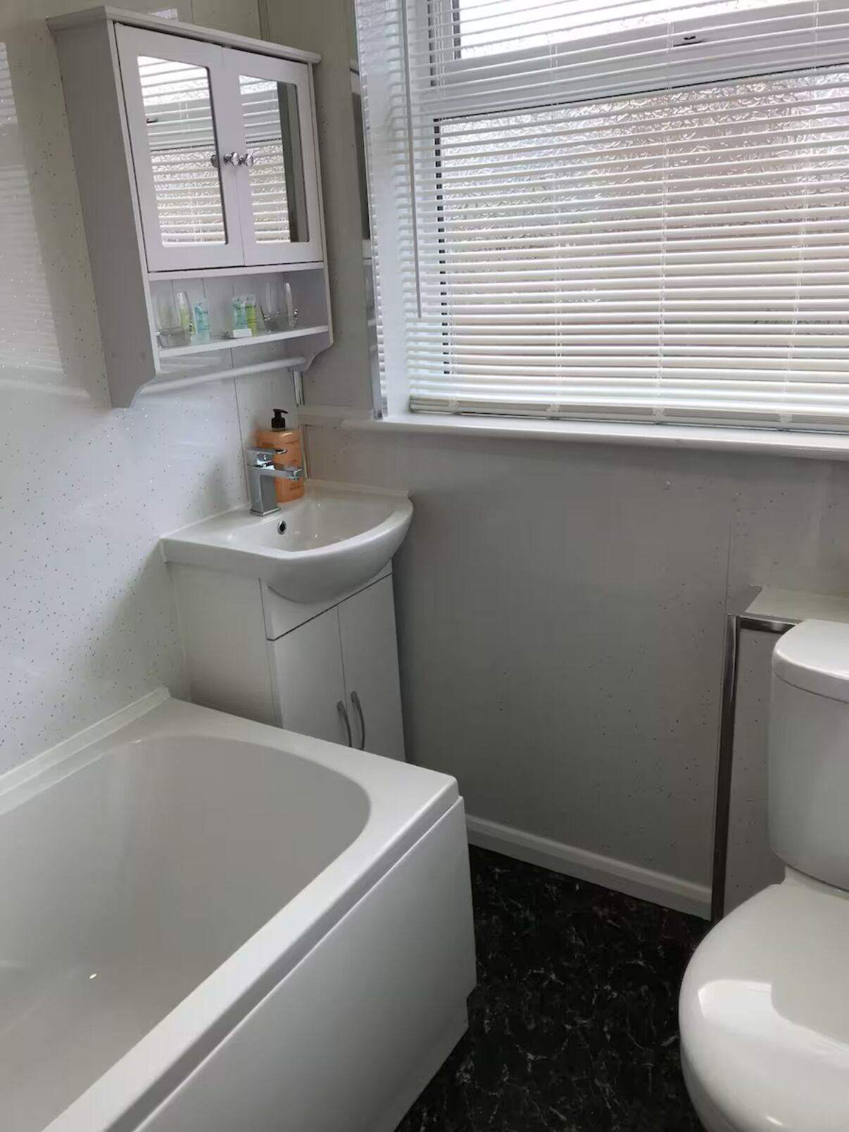A bathroom with a bathtub, a sink, a toilet, and a window with blinds.