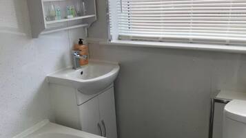 A bathroom with a bathtub, a sink, a toilet, and a window with blinds.