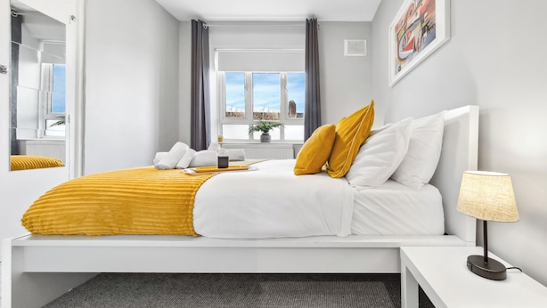 Una habitación de hotel moderna con cama, mesita de noche y ventana con cortinas.