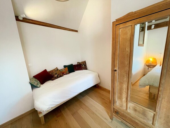 A small, cozy bedroom with a single bed, a wooden wardrobe, and a slanted ceiling.