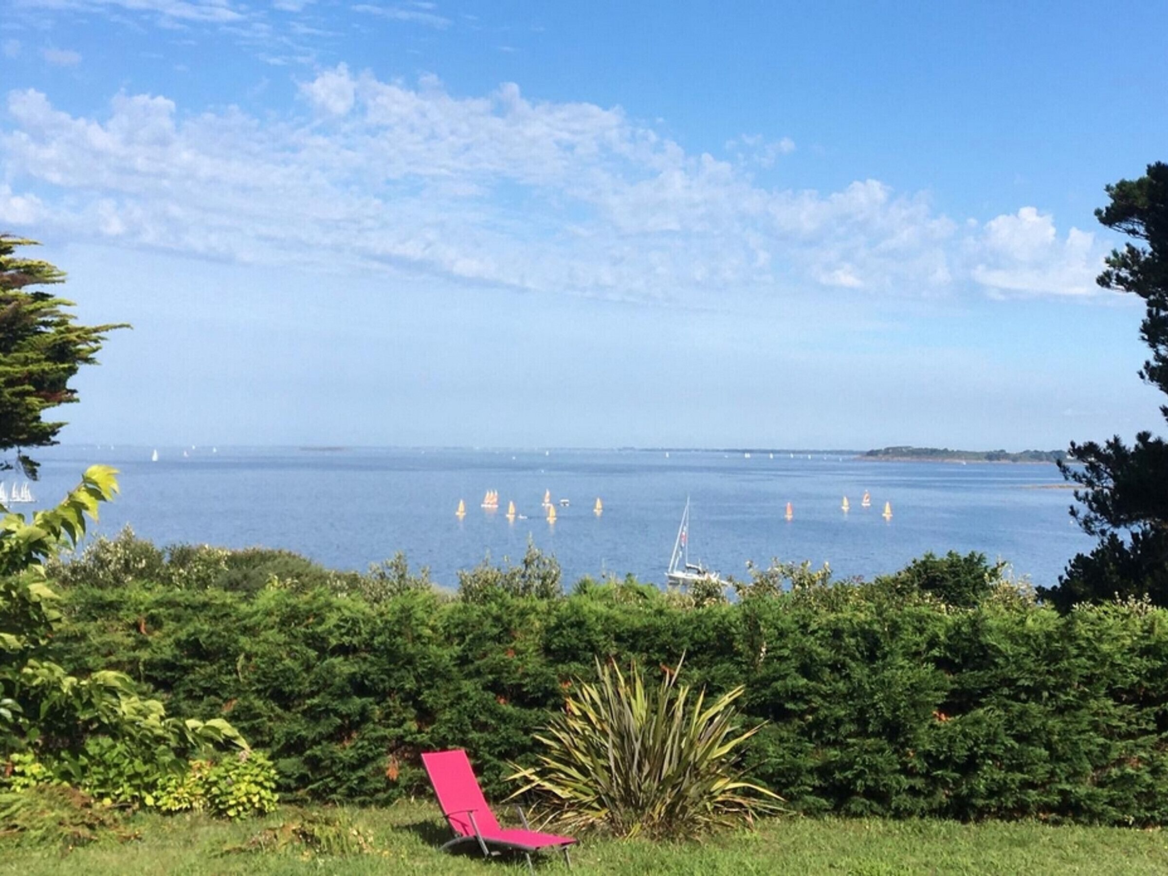 A coastal view with a chair in the foreground, a clear sky, and several boats on the water.