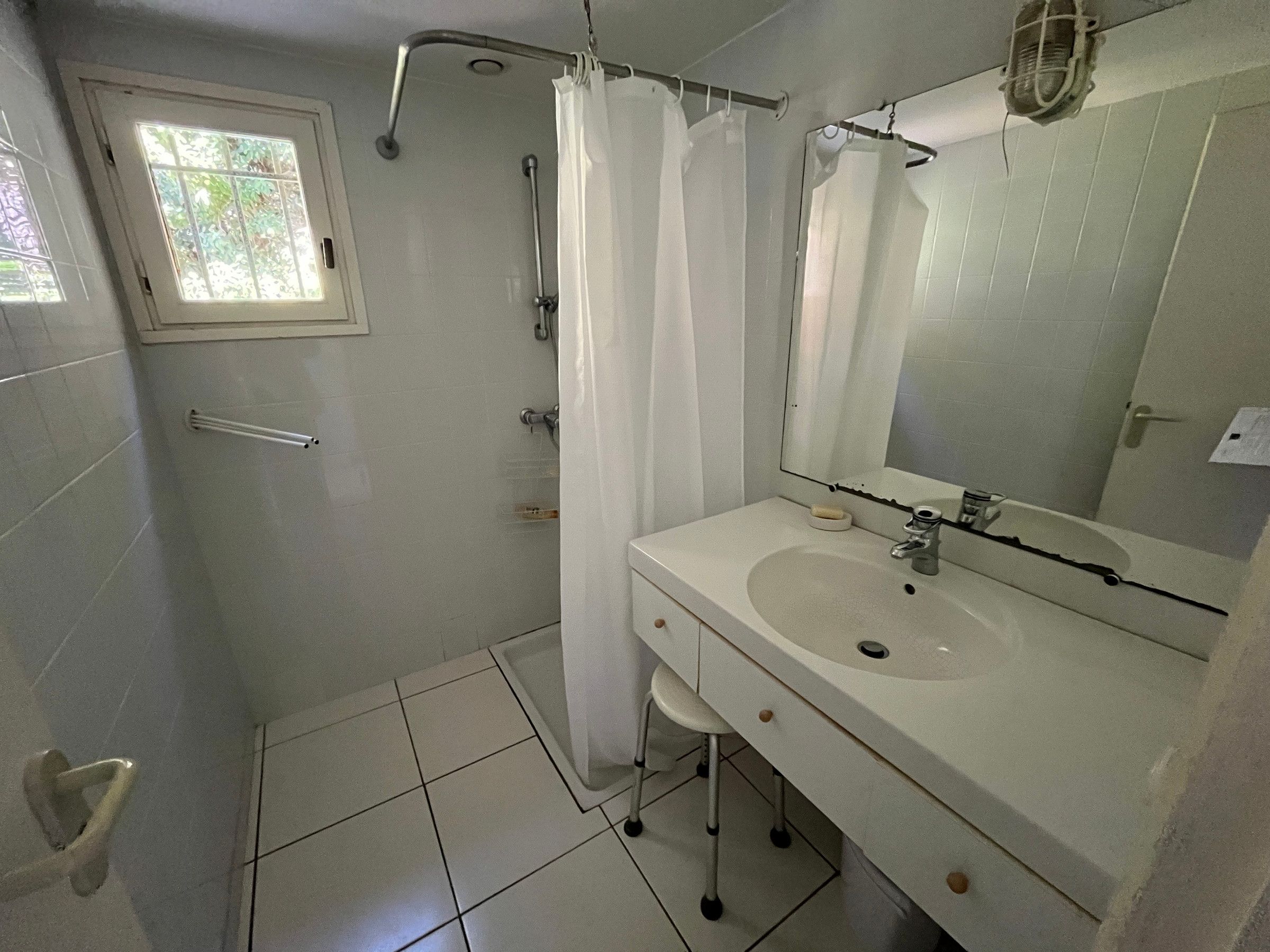 A bathroom with a shower, a sink, a mirror, and a window.
