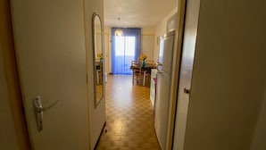 Un couloir carrelé mène à une salle à manger où se trouvent une table et des chaises.