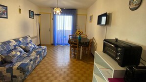 Un salon comprenant un canapé, une table à manger avec des chaises, un téléviseur et une chaîne stéréo.