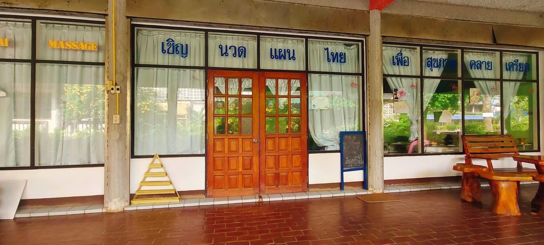 Un salón de masajes con grandes ventanales, puertas de madera y un banco en el exterior.