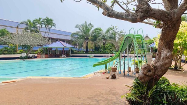 A swimming pool with a green slide, surrounded by palm trees and a covered seating area. - Sinsiamresort (Klaeng)