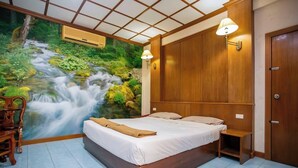 A bedroom with a bed, wooden headboard, bedside table, and a wall mural of a waterfall. - Sinsiamresort (Klaeng)