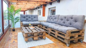 A patio with a wooden bench and a sofa, a small table with a bowl of fruit, and a potted plant.