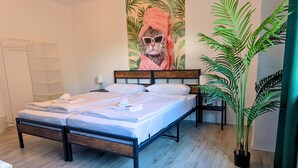 A neatly made bed with white linens and a towel, a wooden headboard, a wall-mounted shelf, and a potted plant.