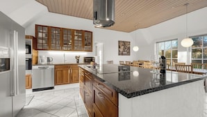 Cozinha moderna com armários de madeira, uma ilha grande, eletrodomésticos de aço inoxidável e uma área de jantar com luz natural.