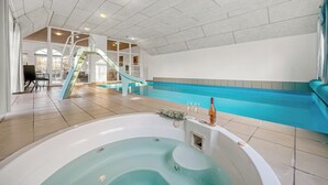 Uma área interna de piscina moderna com hidromassagem, um escorregador e um espaço de estar com mesa e cadeiras.