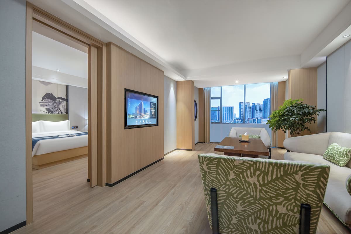 A modern hotel room with a bed, a sofa, a coffee table, and a TV mounted on the wall.