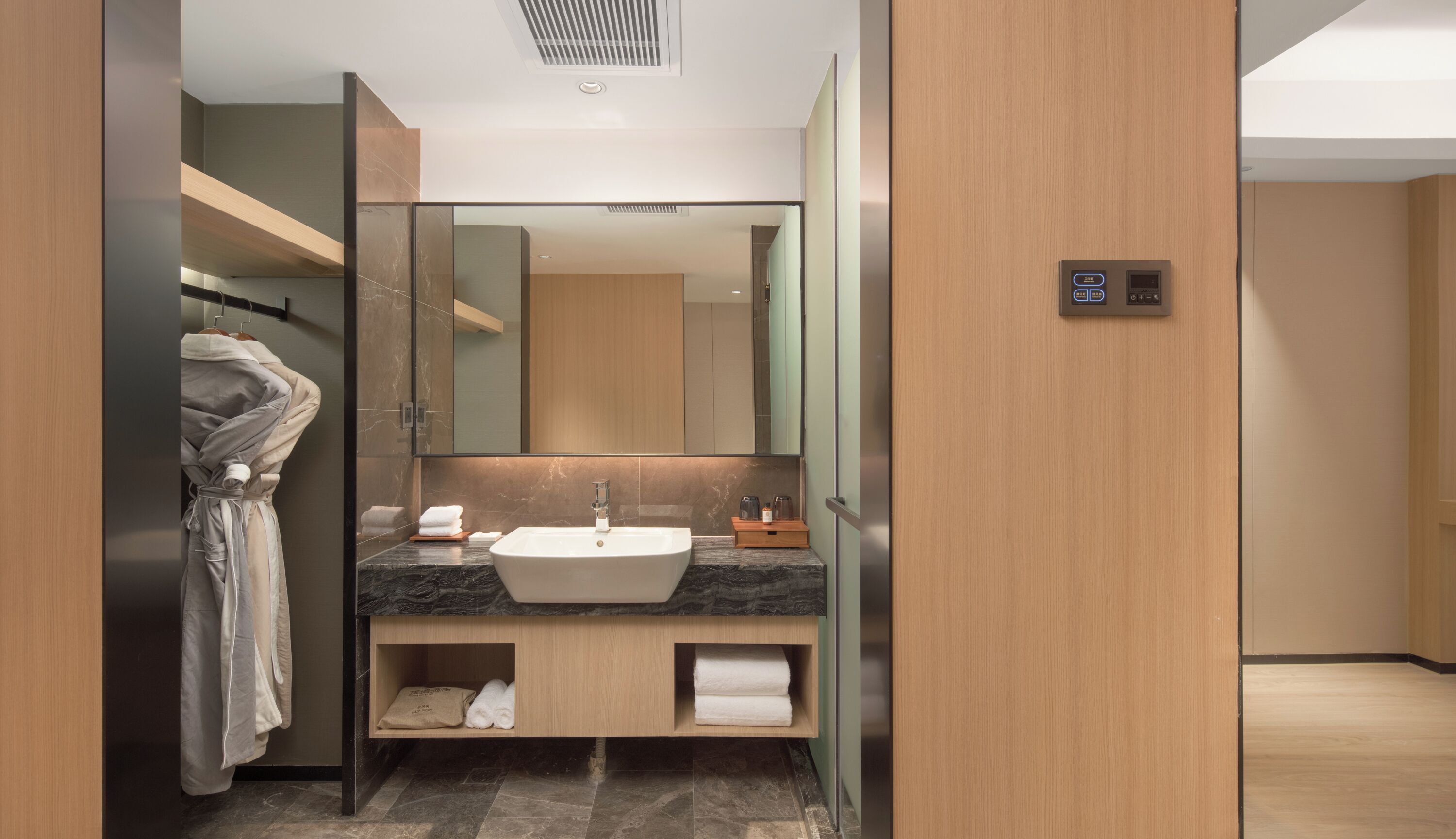 A modern bathroom with a large mirror, a sink, and a robe hanging on a rack.