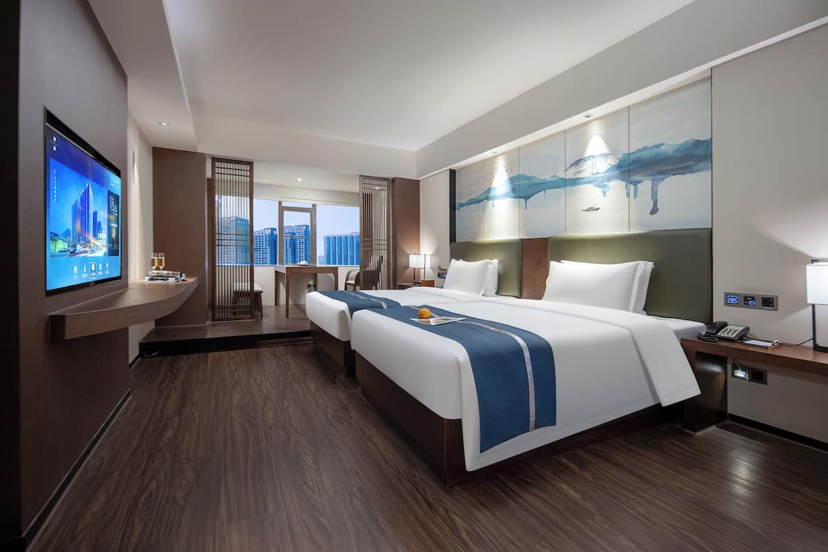 A modern hotel room with a large bed, a desk, a TV, and a city view.