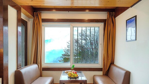 A room with two brown leather sofas, a glass-top table with fruit, a window with curtains, and a framed picture on the wall.