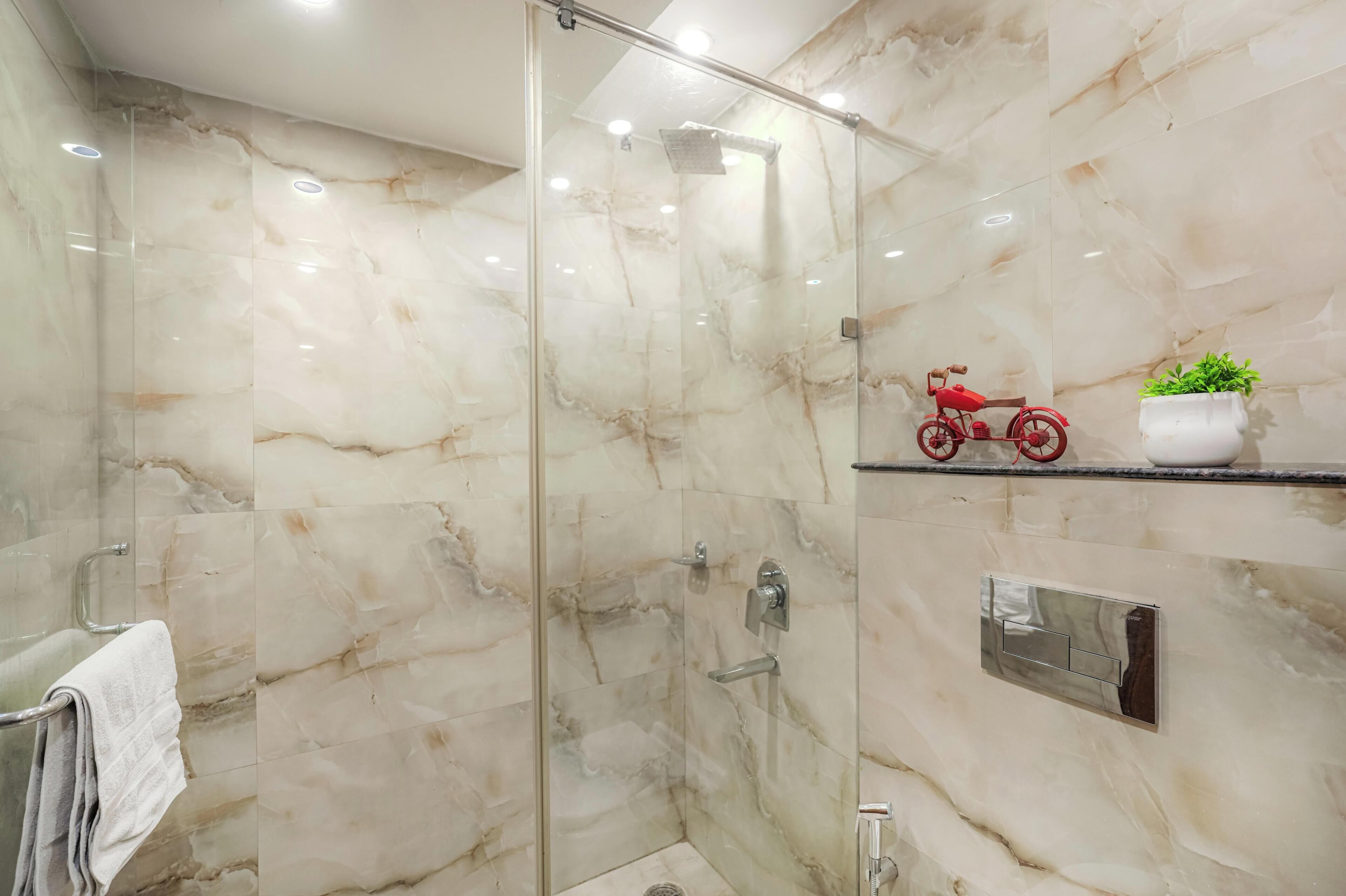 Un bagno moderno con doccia vetrata, pareti in marmo, portasci asciugamani, una macchinina rossa e una pianta in vaso.