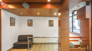 A reception area with a sofa, glass railing, wooden ceiling, framed pictures, and a window with a plant.