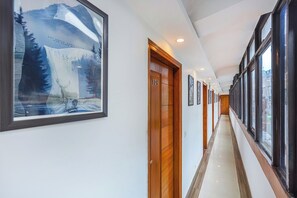 A hallway with wooden doors, framed artwork, and large windows.