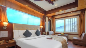 A hotel room with a large bed, a sofa, a small table with fruit, and a window with a mountain view.