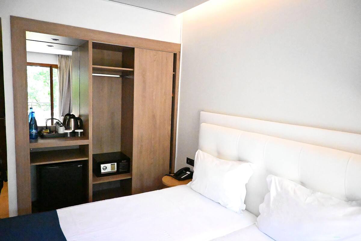 A hotel room with a bed, a wardrobe, a desk with a phone, and a small refrigerator.
