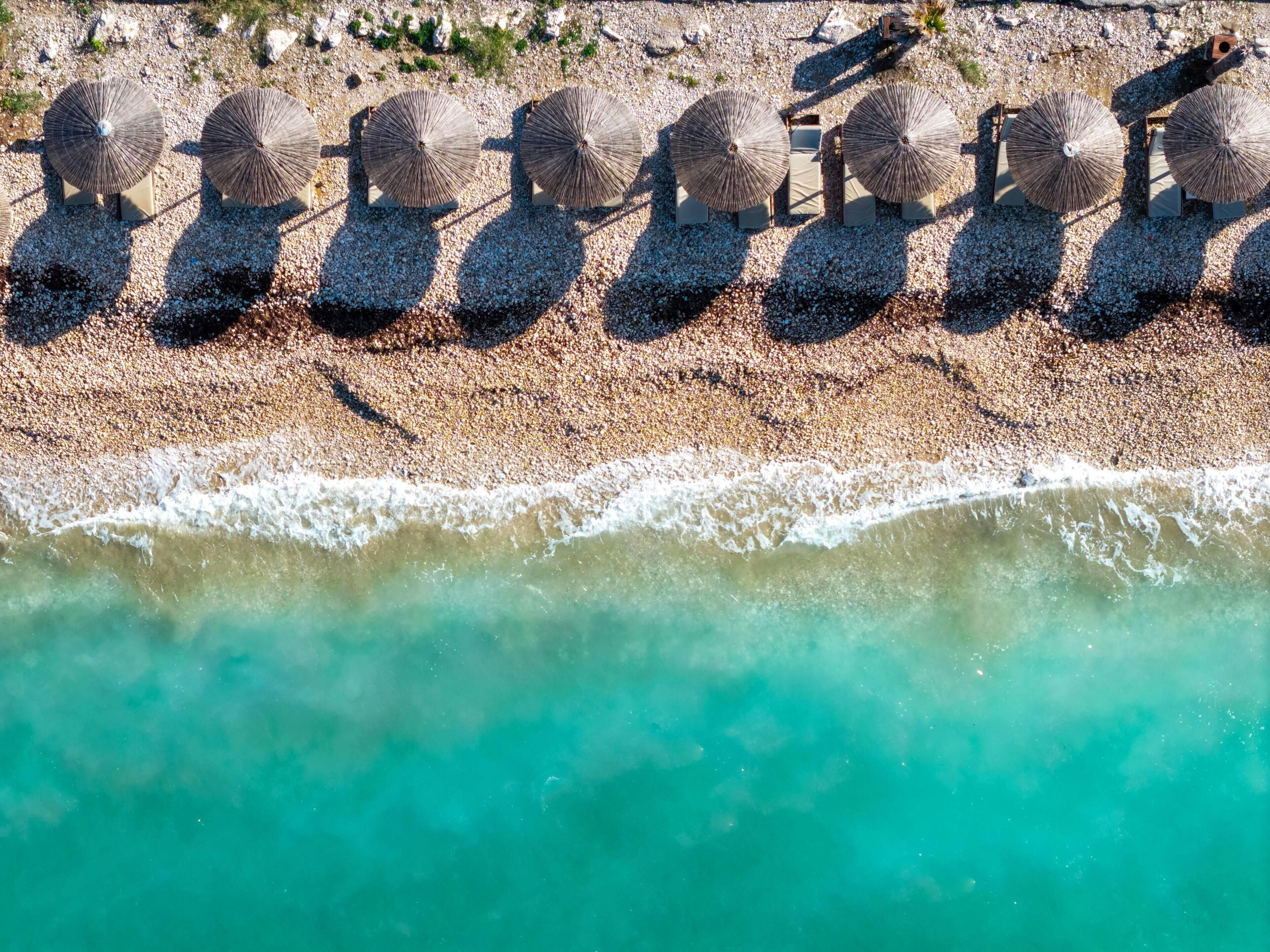 An aerial view of a beach with multiple sun loungers and umbrellas aligned in a row.