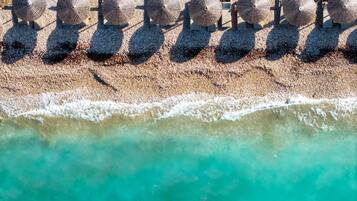 An aerial view of a beach with multiple sun loungers and umbrellas aligned in a row.