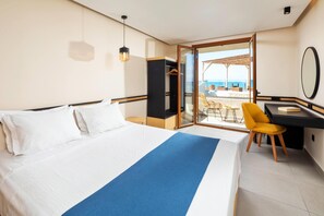 A hotel room with a bed, a desk, a chair, and a view of the sea.