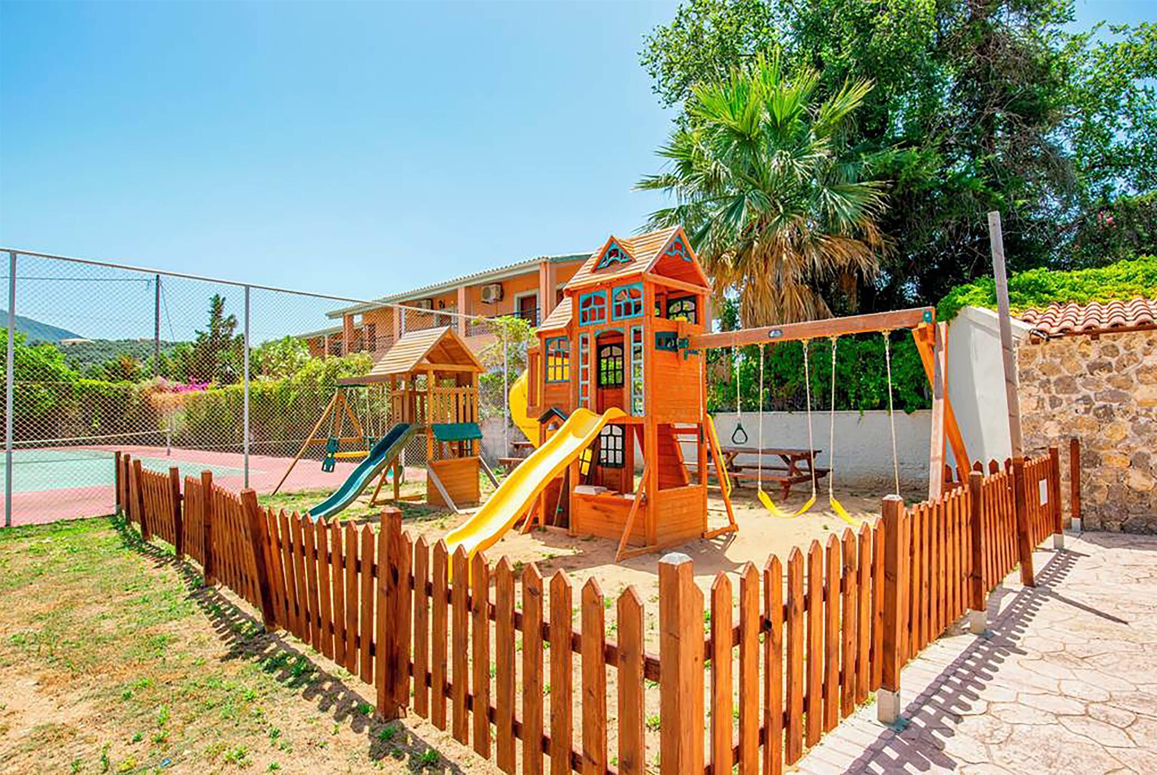 A playground with a wooden fence, a slide, and a swing set.