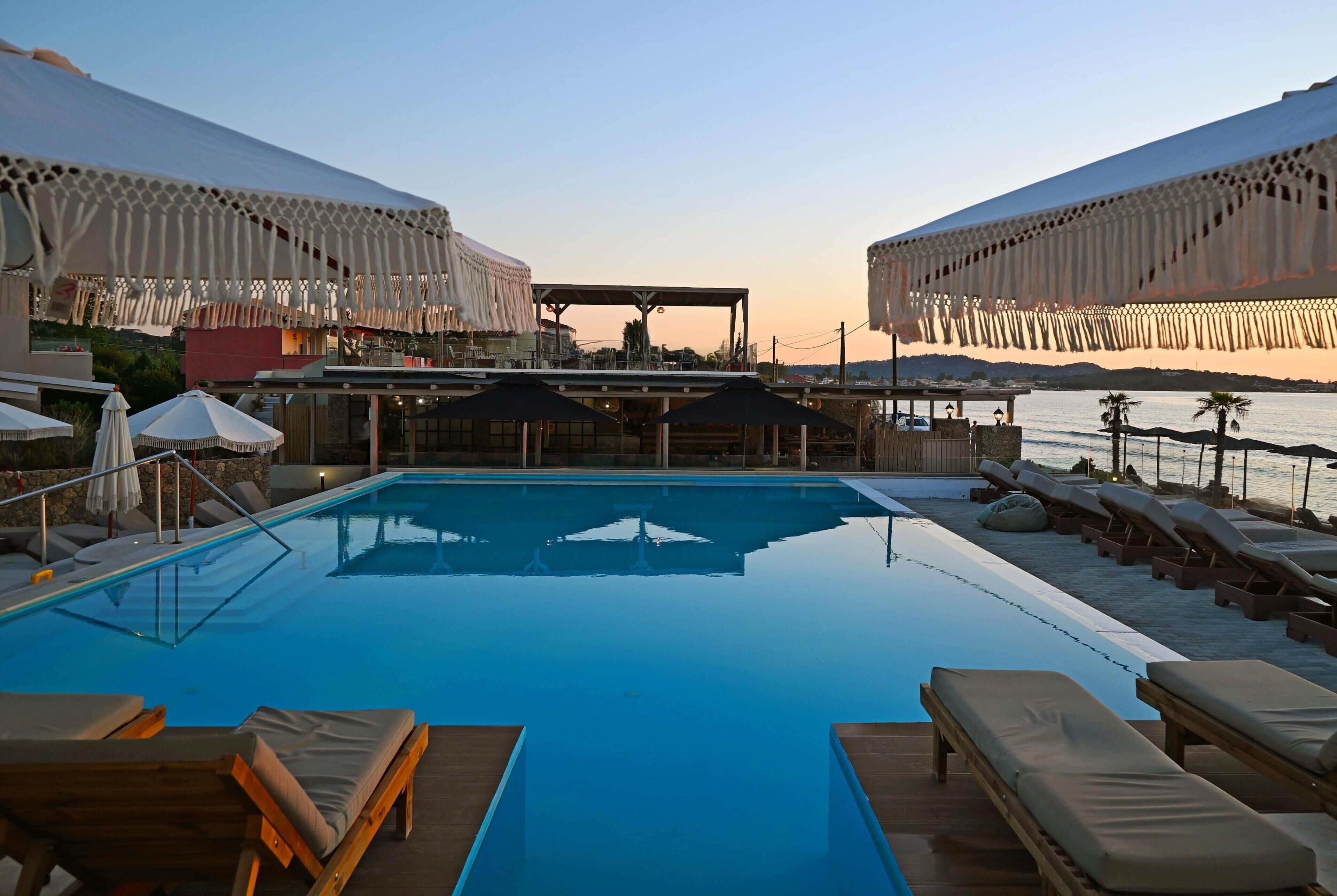 Zona de piscina con sillones de descanso, sombrillas y vistas al agua.