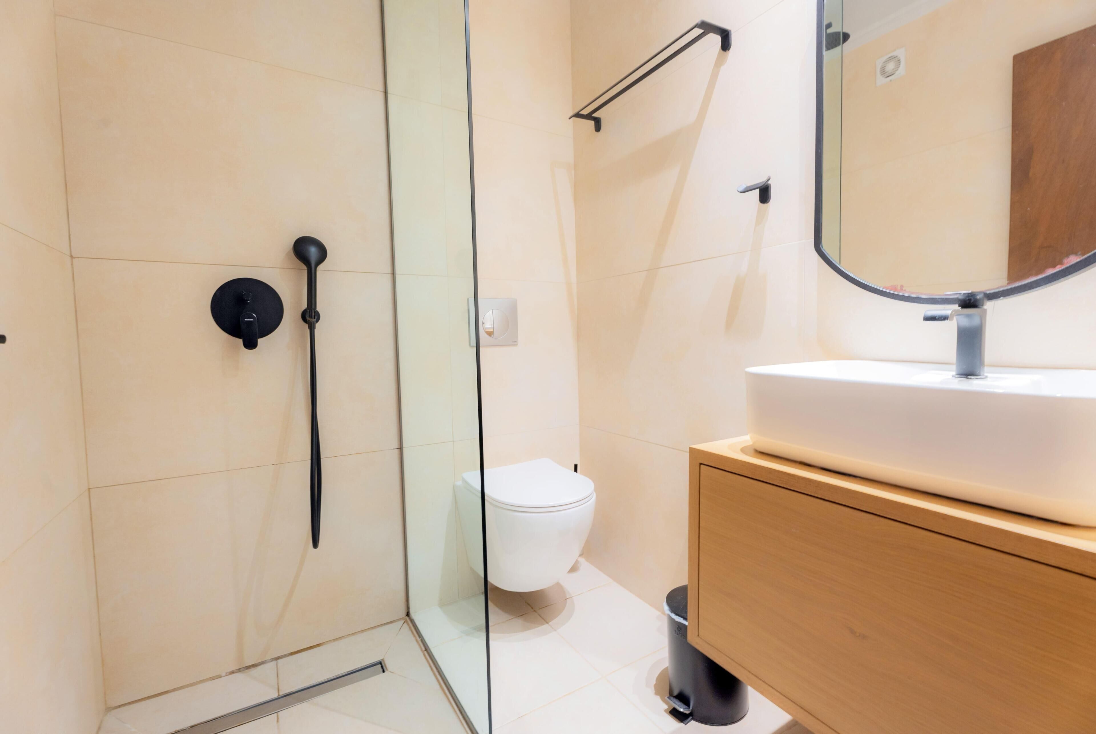A modern bathroom with a glass shower enclosure, a white toilet, and a wooden vanity with a sink.