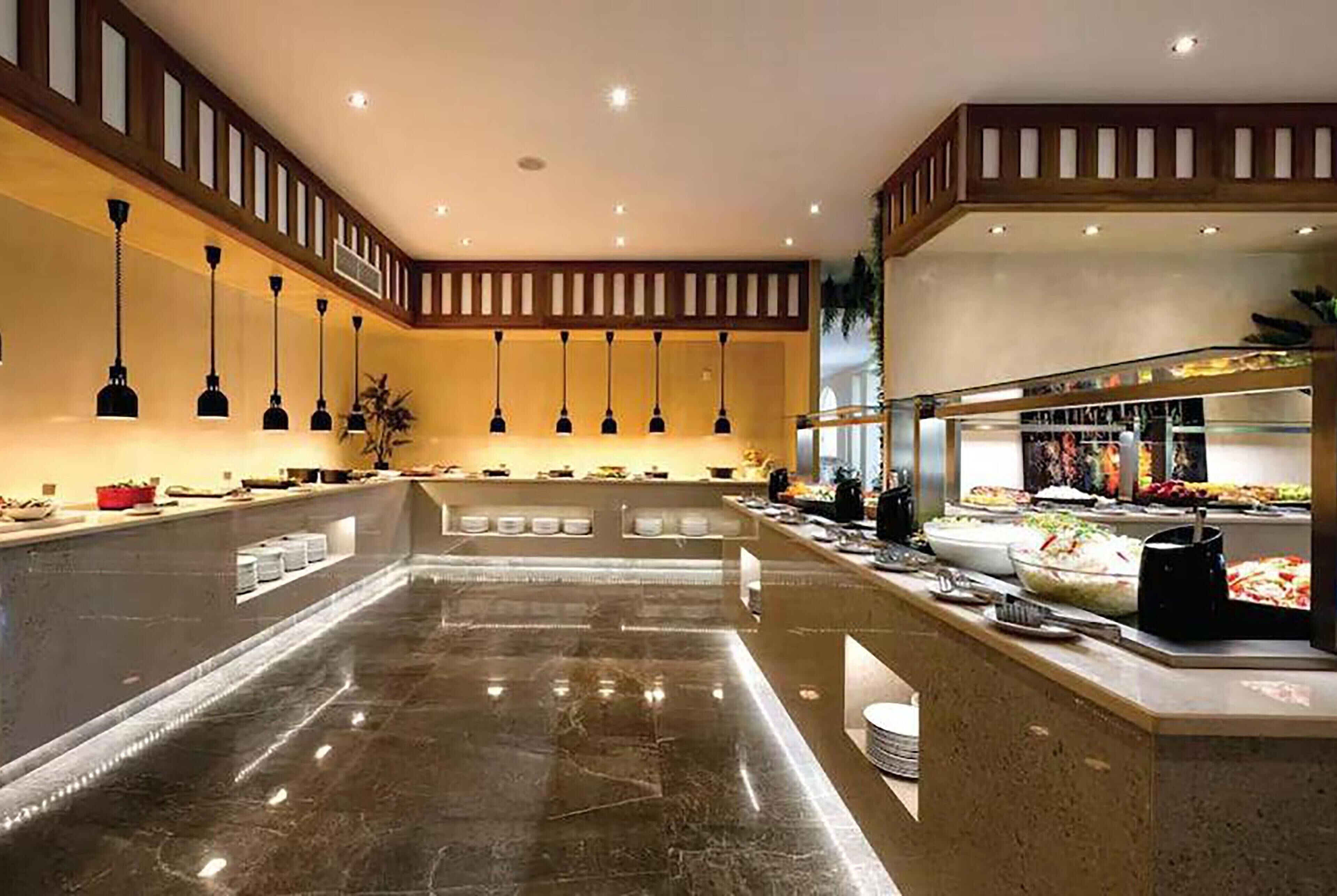 Un vestíbulo de hotel con piso de mármol, mostrador de buffet, iluminación colgante y diseño de techo de madera.
